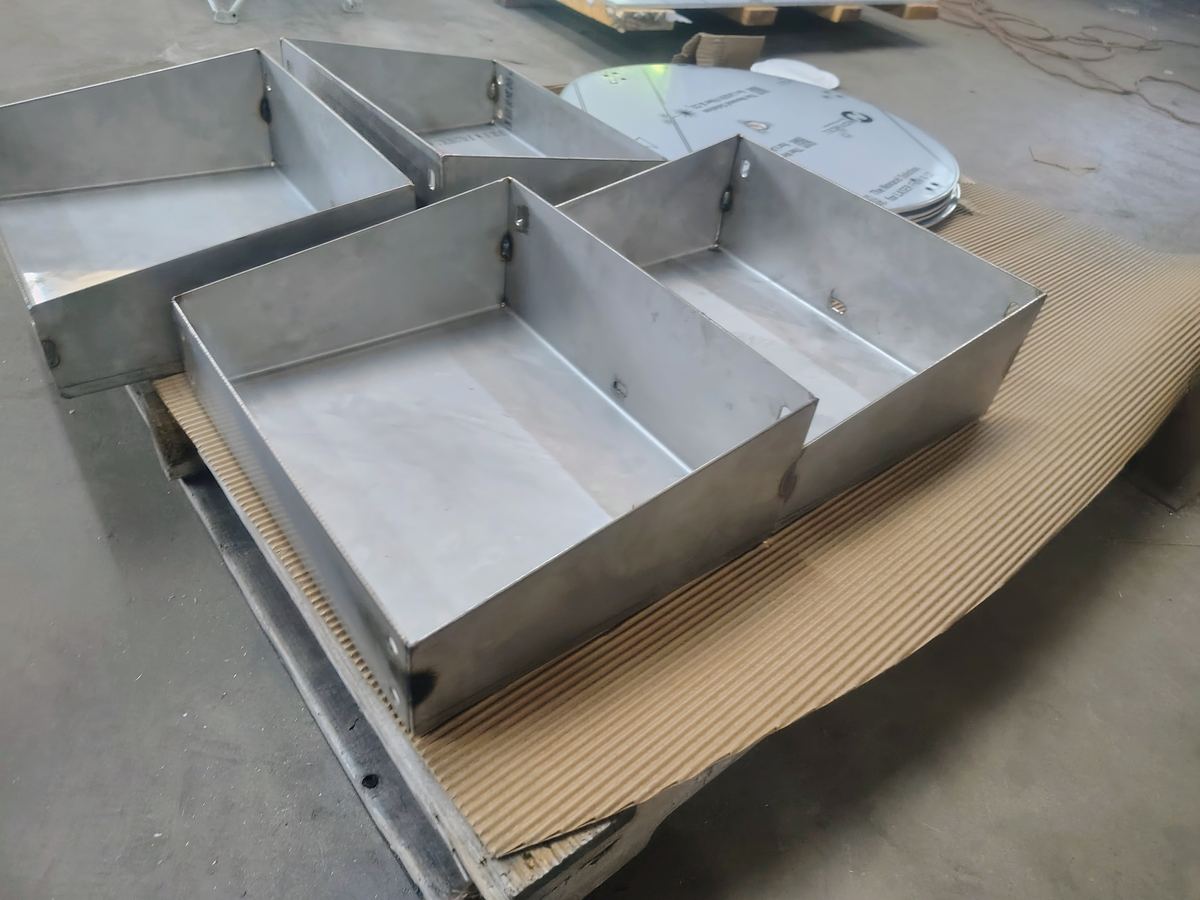 Formed sheet metal trays stacked on cardboard in the shop